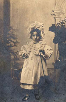 Little girls' clothing could be highly decorative, like the frilly bonnet and dress with pom-poms shown in this photograph. This three-year old girl was placed with foster parents in the Devonshire countryside. Finding foster homes for children was always a key area of the Waifs and Strays' Society's work.