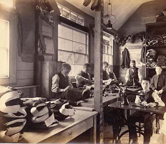 Larger workshops were run as a production line, with several different jobs involved. The boys on the left are hand sewing, while the boy in the foreground is using a treadle sewing machine. 