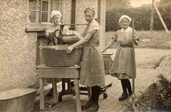 Before the advent of modern technology in homes, all laundry and washing was done manually.  These girls are using a hand-turned mangle to squeeze water out of their washing. 